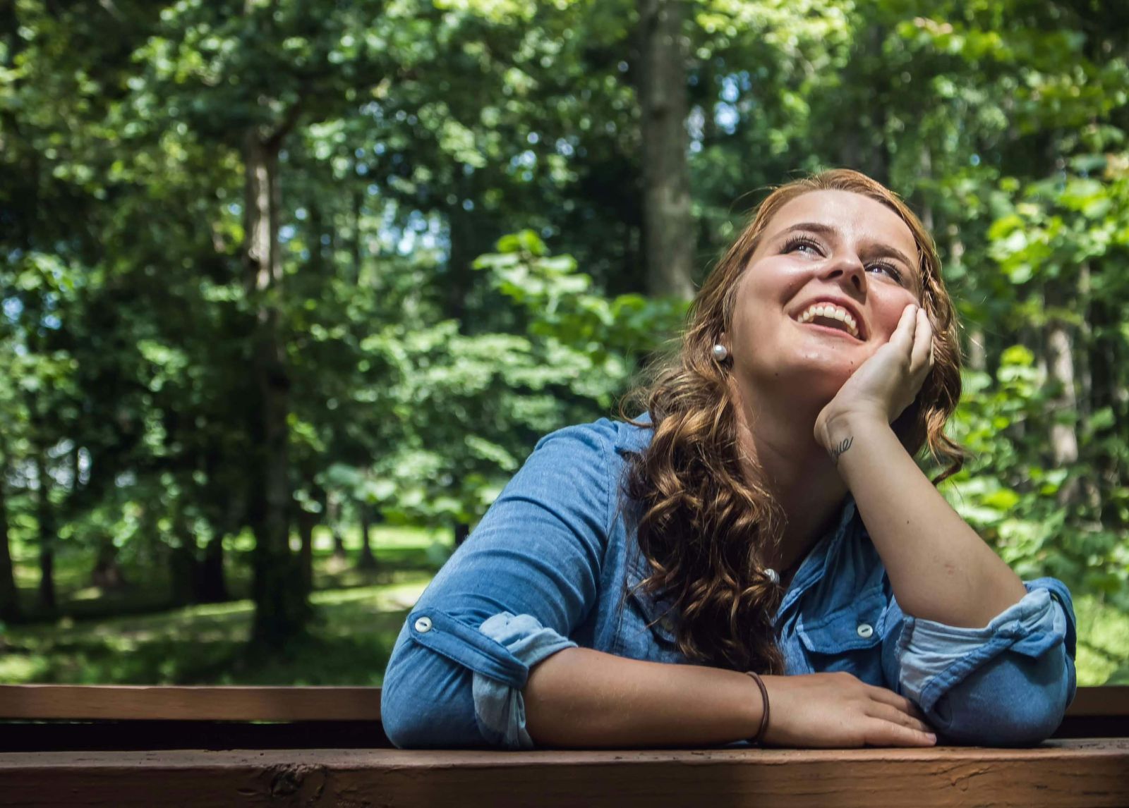 A cheerful woman sits on a bench in the woods, enjoying the tranquility of nature with a bright smile.